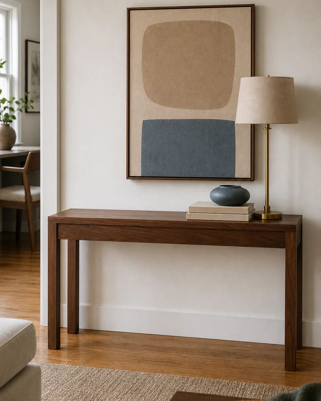 A direct front view of a warm walnut console table against a warm-white wall with the right two thirds of the top styled with a tall slim brass lamp a stack of two blank-cover books and a low sage vessel and the left one third of the console top kept completely empty as visible breathing room