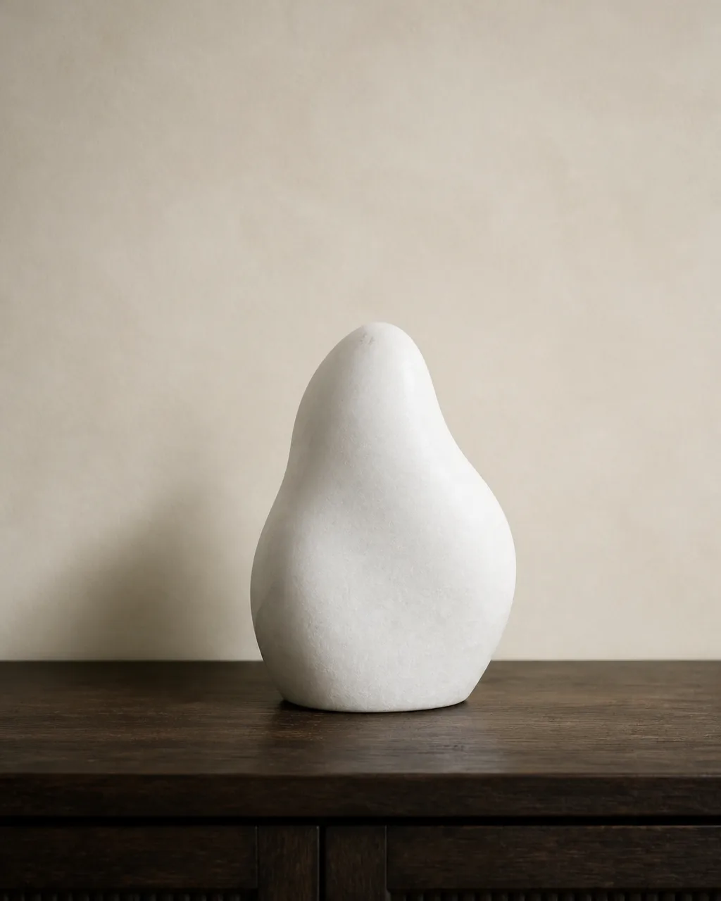 A smooth white stone abstract sculptural form centered on a dark wood console table with generous empty space on both sides and warm natural light