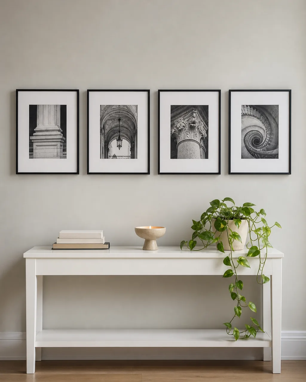 Four black-and-white architectural photographs in thin black metal frames hung in a horizontal row above a white console table with books and a pothos plant